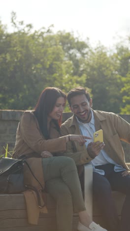 Vertikales-Video-Eines-Muslimischen-Paares-Bei-Einem-Date,-Das-Im-Stadtpark-Im-Freien-Sitzt-Und-Gemeinsam-Auf-Sein-Mobiltelefon-Schaut-1